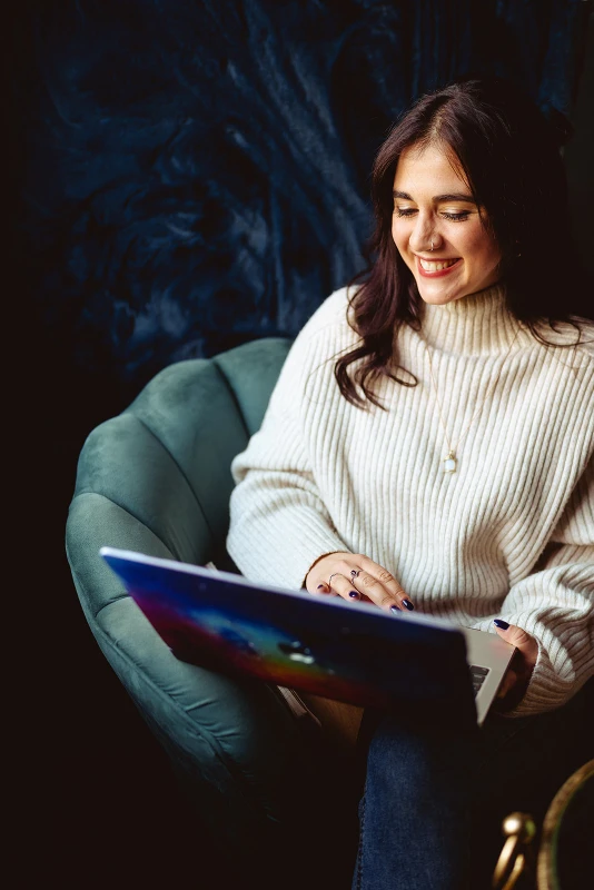 Woman smiling while using a laptop in a chair