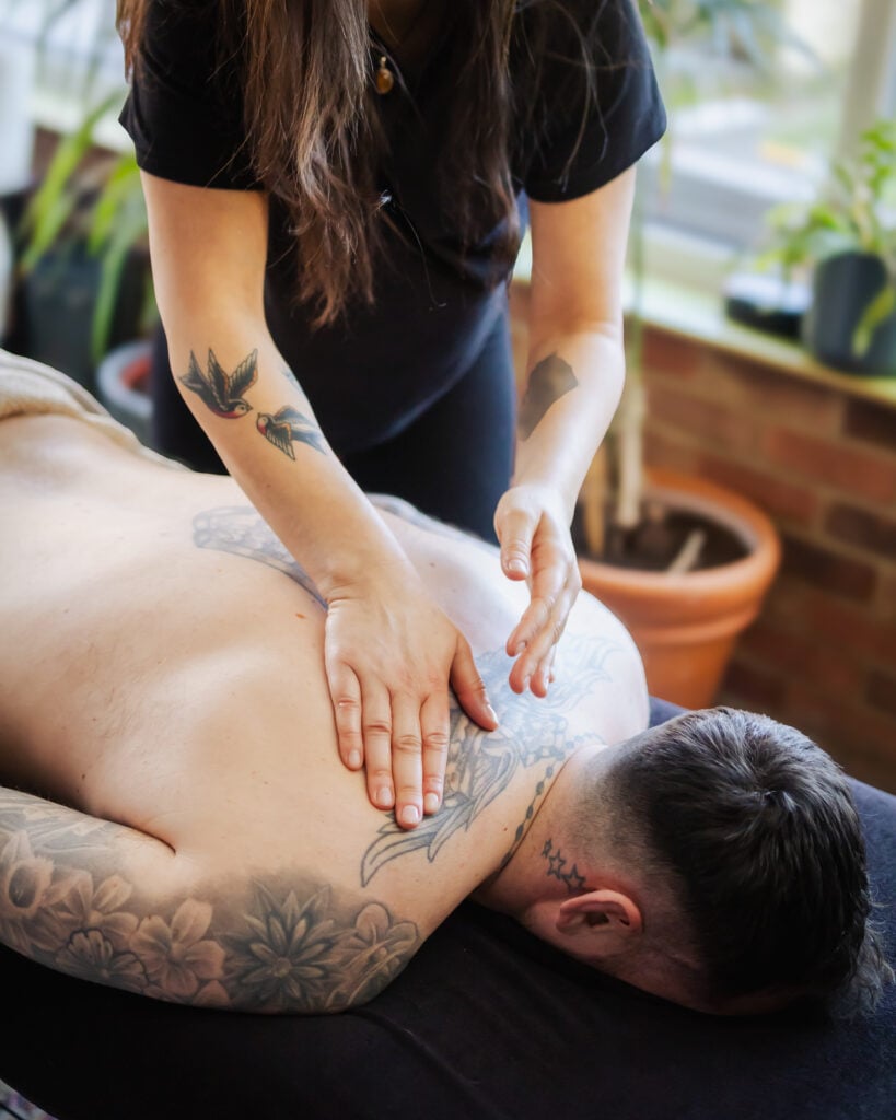 Person receiving back massage with arm tattoos.